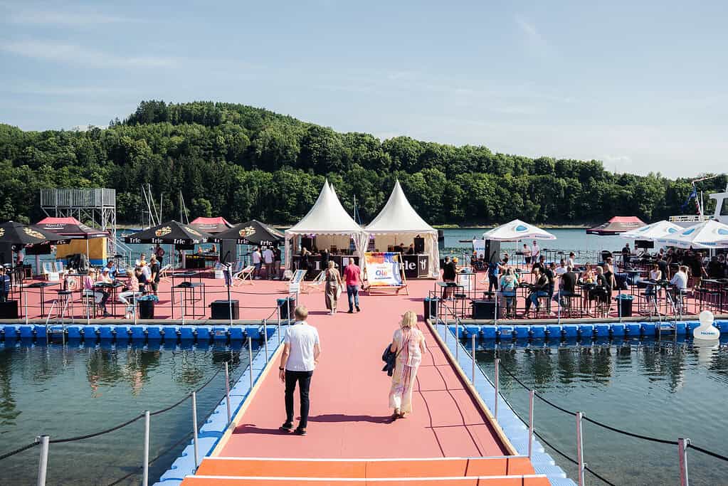 Gemütlicher Blick auf das Biggesee Open Air 2026 am Wasser mit Menschen, Zelten und Veranstaltungen bei schönem Wetter.