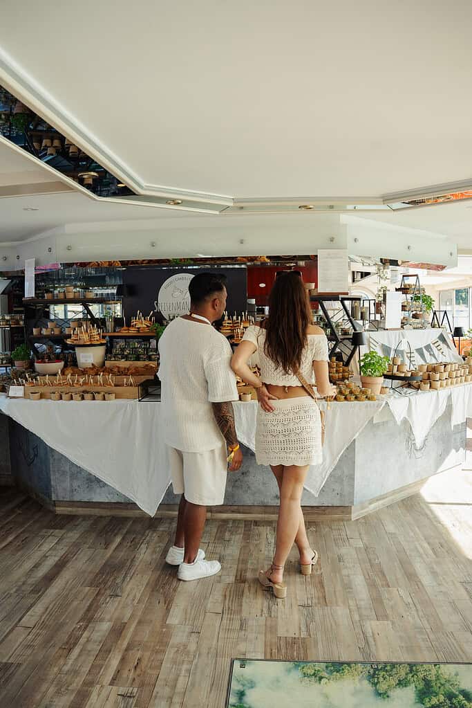 Schwarz-weißer Stand mit trendigem Event-Bereich, Menschen bei einem Food- und Lifestyle-Festival, sommerlicher Look mit Strandkleidung, Atmosphäre von Biggesee Open Air 2026, moderne Event-Location, Genuss und Gemeinschaft.